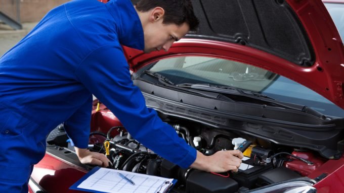 Mechanic In Uniform Repairing Car Side view of young mechanic in uniform repairing car